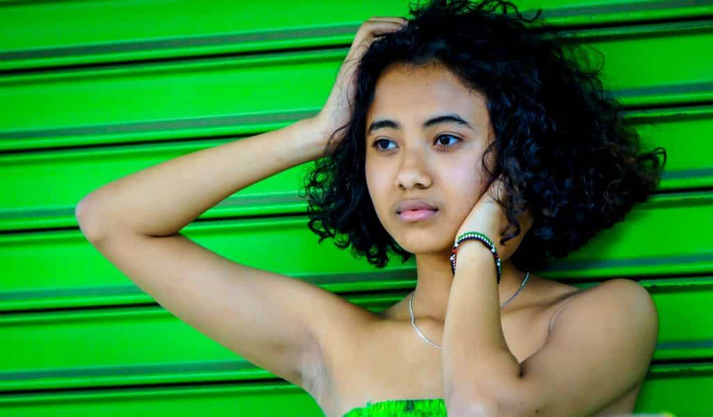 Imagem de uma linda mulher negra encostada em um portão pintado na cor verde.