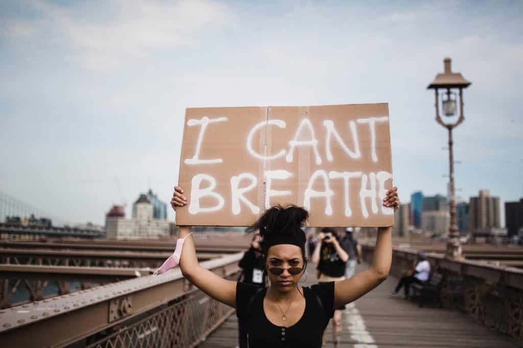 Mulher negra em um protesto de rua, segurando um cartaz com os escritos "I can't breathe" ou "eu não consigo respirar", em inglês.