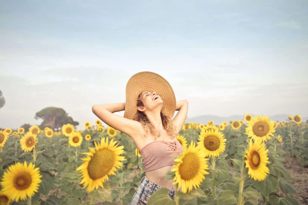 Mulher de chapéu com os braços abertos em um campo de girassóis.