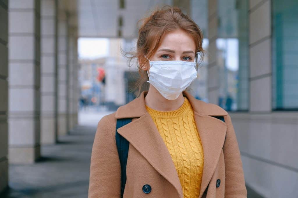 Mulher em ambiente aberto, usando roupas de frio e uma máscara de proteção facial.