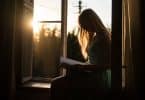Mulher lendo ao lado da janela com a luz do pôr do sol