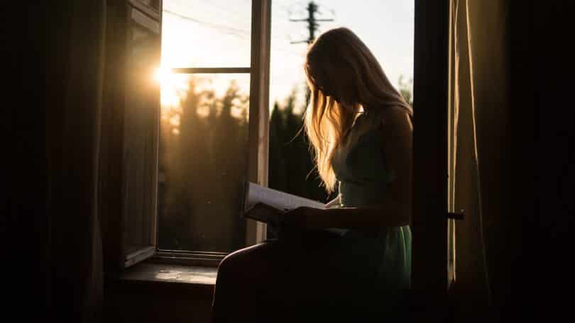 Mulher lendo ao lado da janela com a luz do pôr do sol