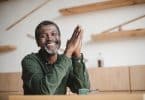 Homem de meia idade sentado à mesa de uma cafeteria, sorrindo.