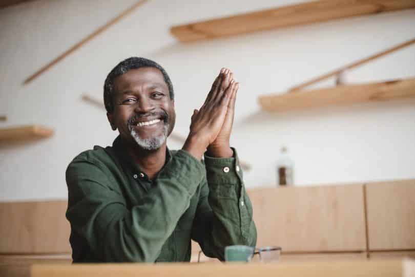 Homem de meia idade sentado à mesa de uma cafeteria, sorrindo.