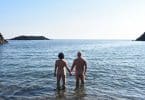 Casal de costas em praia de nudismo de mãos dadas