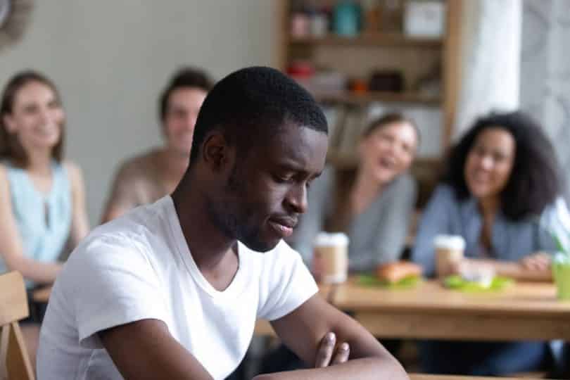 Grupo de pessoas ao fundo rindo de homem negro em foco