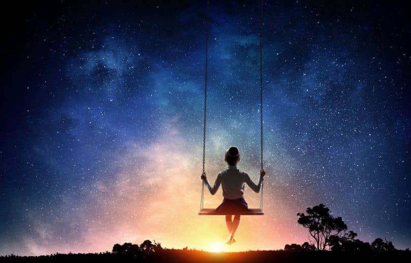 Silhueta de menina em balanço olhando céu estrelado