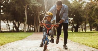 Pai negro ensinando filho a andar de bicicleta ao ar livre