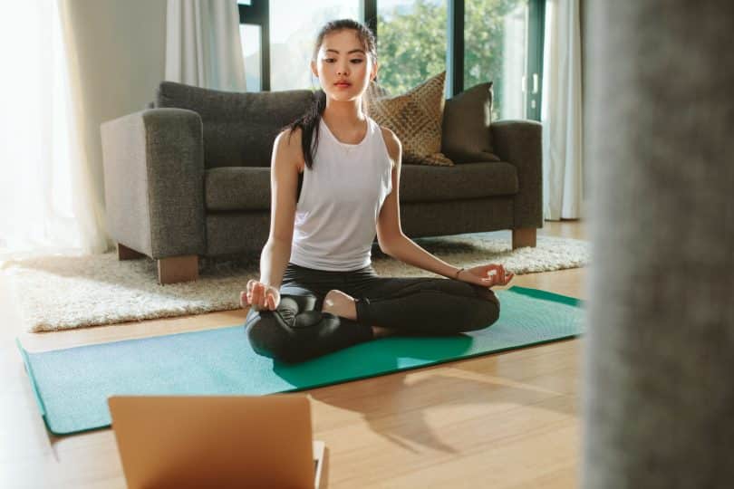 Mulher sentada em pose de yoga olhando para o notebook.