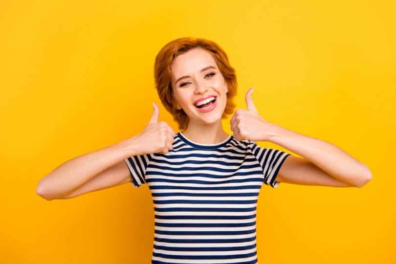 Mulher sorrindo fazendo joia com as mãos em fundo amarelo