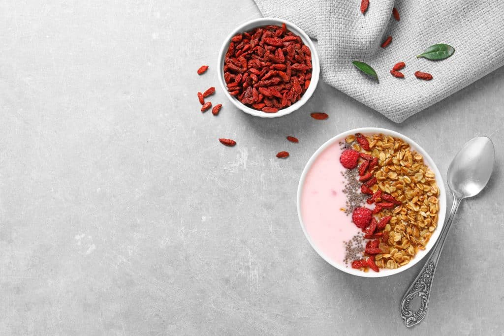 Pote com iogurte, cereal e goji berry ao lado de uma colher