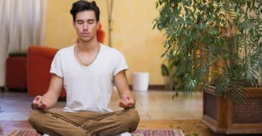 Homem sentado em tapete com olhos fechados meditando