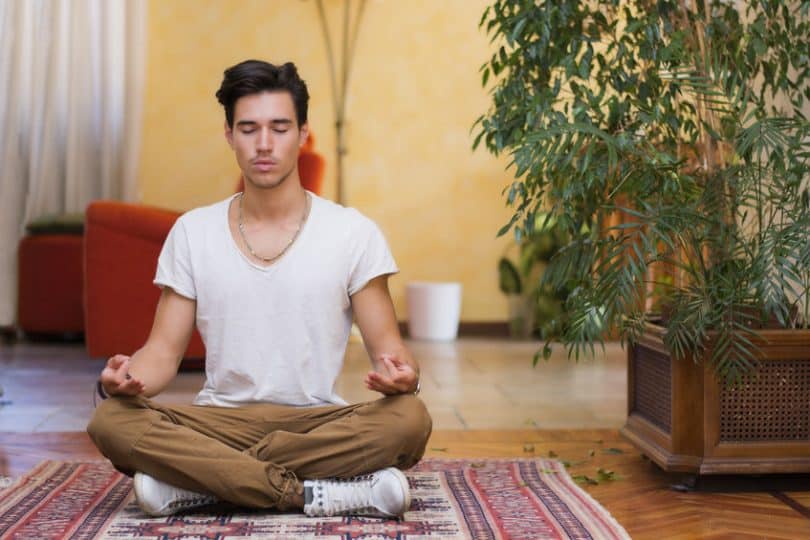 Homem sentado em tapete com olhos fechados meditando