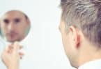 Homem branco segurando um espelho olhando à si mesmo.