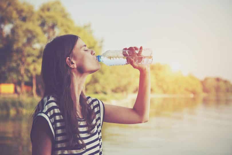 Mulher branca bebendo água da garrafa numa praça