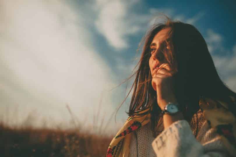 Mulher branca com cabelos lisos num campo e mão levada à boca