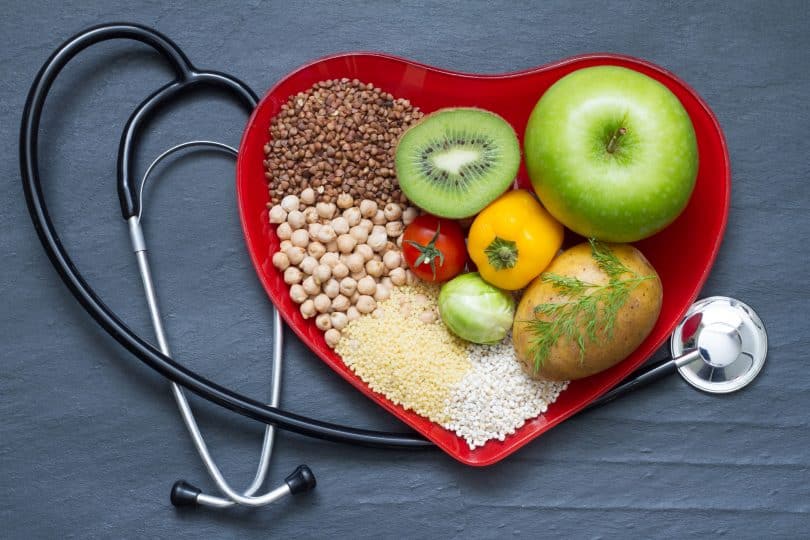 Pote em formato de coração com frutas e cereais, ao lado de um estetoscópio.