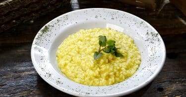 Imagem de um prato branco com risoto servido de cor amarela enfeitado com um broto verde.