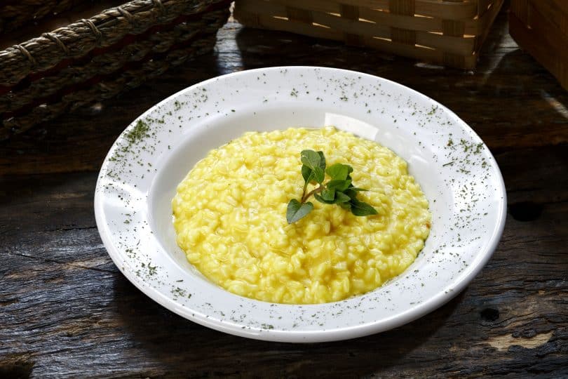 Imagem de um prato branco com risoto servido de cor amarela enfeitado com um broto verde.
