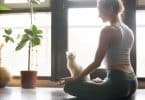 Mulher sentada no chão ao lado de seu gato, meditando.