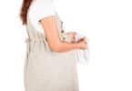 mulher grávida de lado olhando para uma calcinha branca que está em suas mãos.