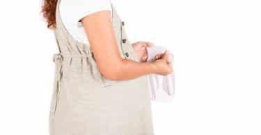 mulher grávida de lado olhando para uma calcinha branca que está em suas mãos.