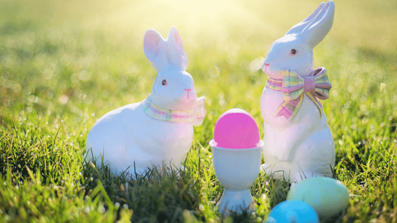 Coelhos de porcelana em um gramado. Alguns ovos coloridos está no meio deles