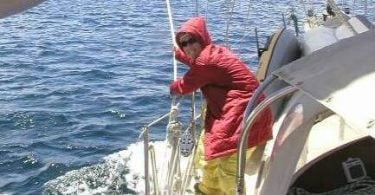Autora usando um casaco grande vermelho e óculos de sol enquanto veleja.