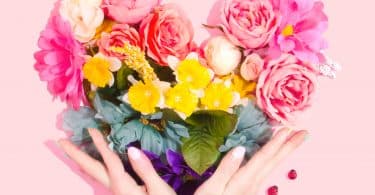 Pessoa contornando com suas mãos um coração feito de flores