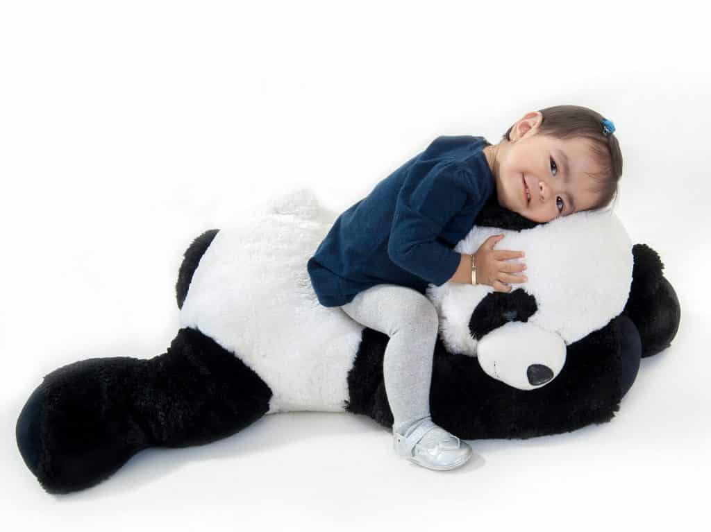 Imagem de uma linda menininha sentada sobre o seu grande urso panda feito de pelúcia.