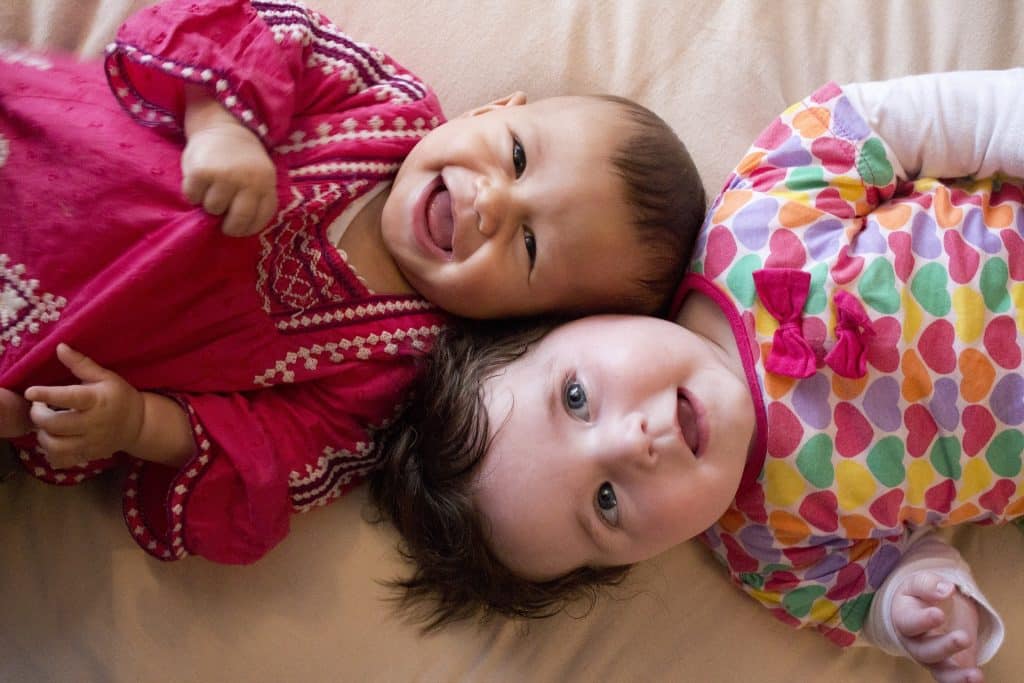 Imagem de duas bebês sorrindo e deitadas sobre uma cama.