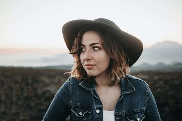 Mulher com chapéu olhando para o lado com campo ao fundo