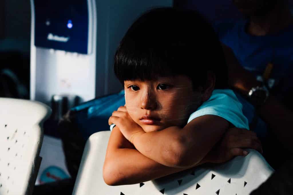 Criança apoiada em uma cadeira olhando para frente com tristeza