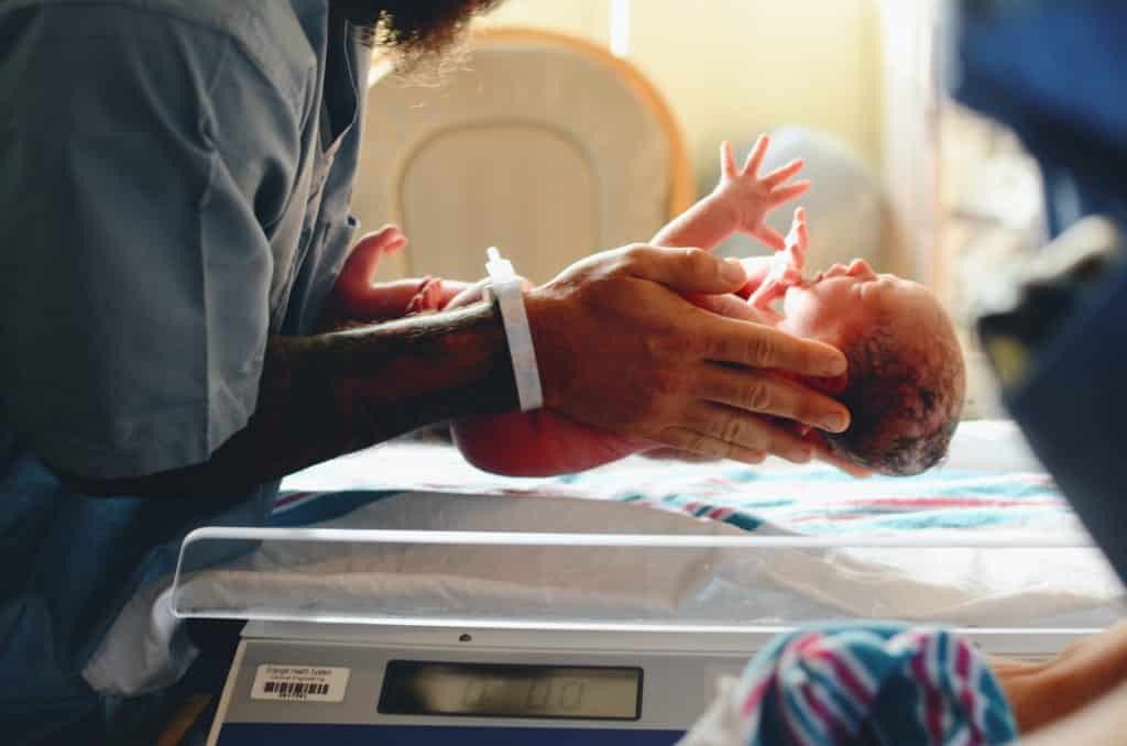 Homem colocando um bebê recém nascido em uma balança própria para a pesagem do mesmo.