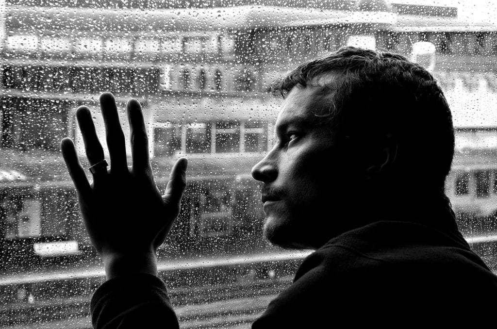 Imagem preto e branco de um homem solitário e depressivo olhando para a janela em um dia chuvoso.