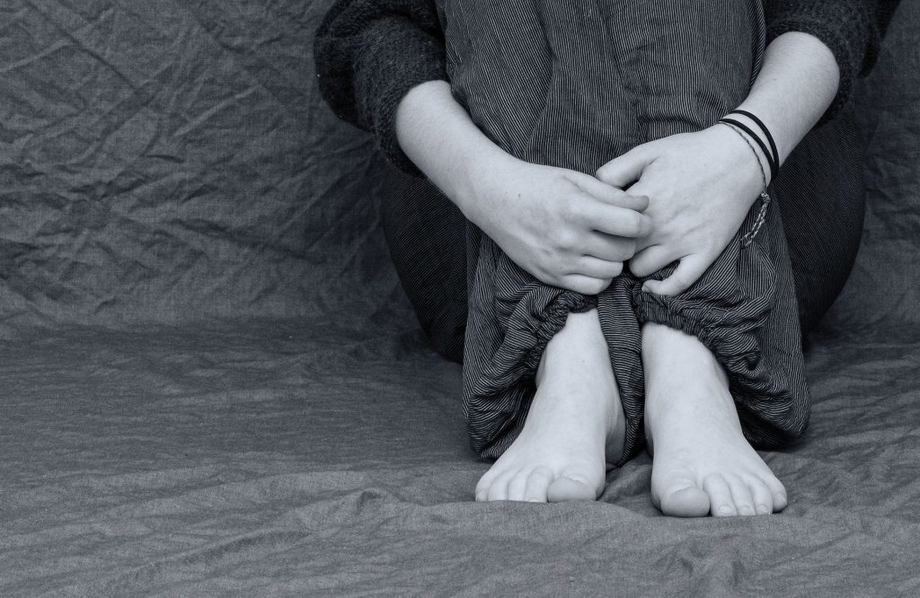 Imagem preto e branco de uma pessoa sentada no chão. Ela está triste e depressiva.