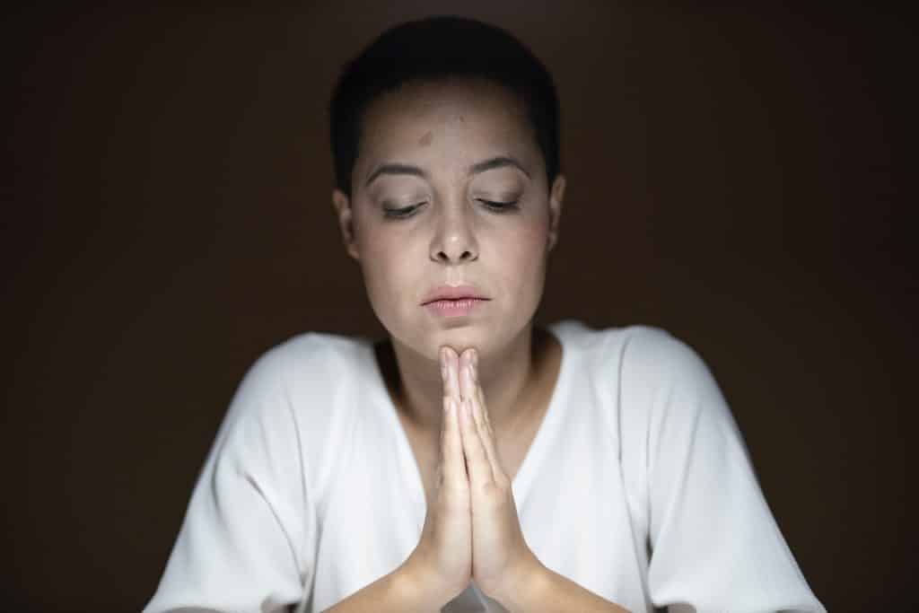 Mulher com os olhos fechados e as mãos unidas, rezando.