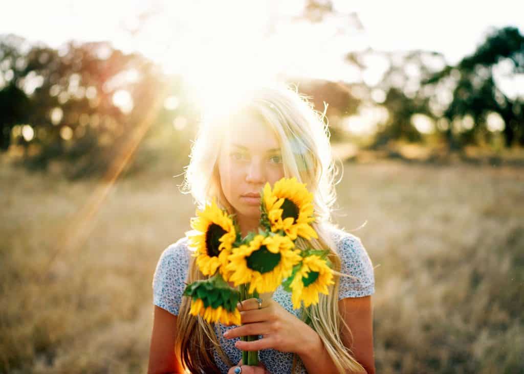 Mulher em um campo de gramado segurando flores de Girassol