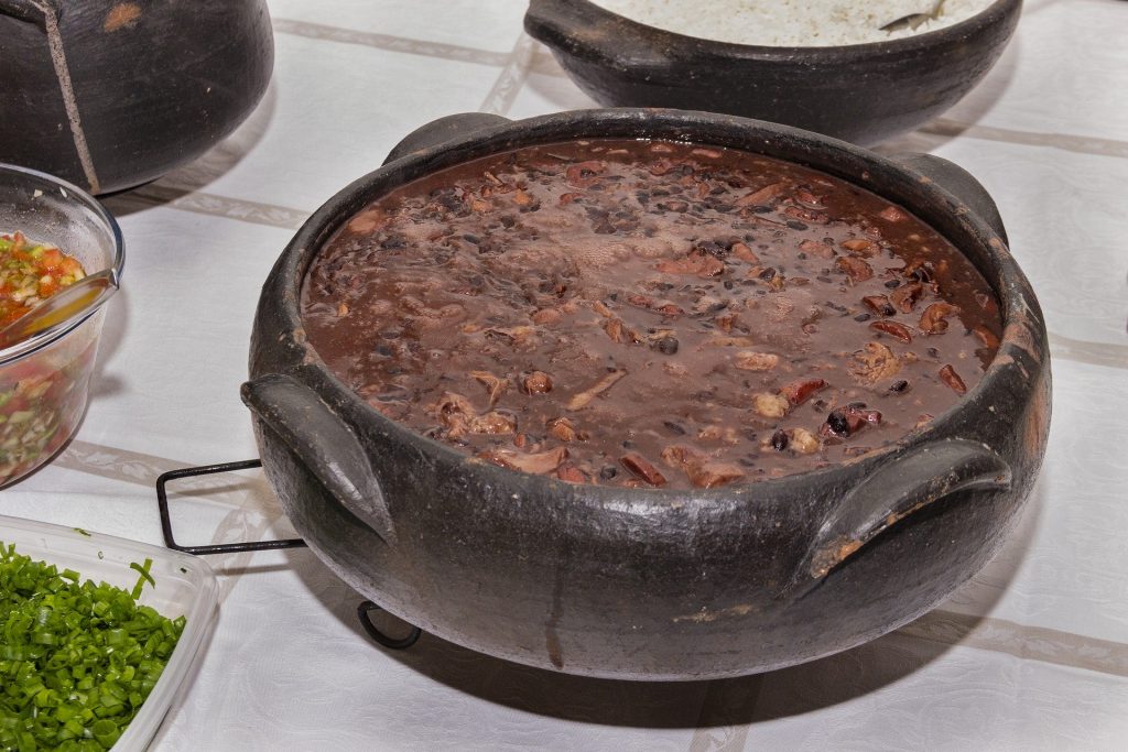 Imagem de uma linda e saborosa feijoada vegetariana disposta em uma cumbuca de barro sobre uma mesa.