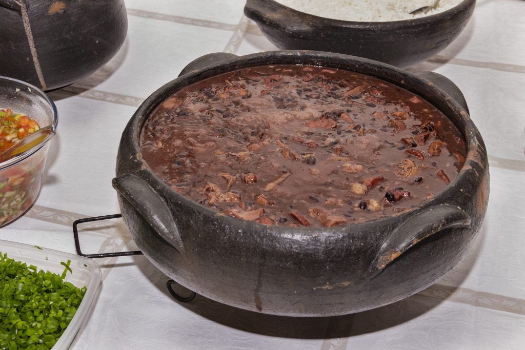 Imagem de uma linda e saborosa feijoada vegetariana disposta em uma cumbuca de barro sobre uma mesa.
