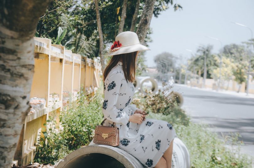 Imagem de uma garota bem vestida e elegante. Ele está sentada olhando para rua. Parece estar bem desanimada.