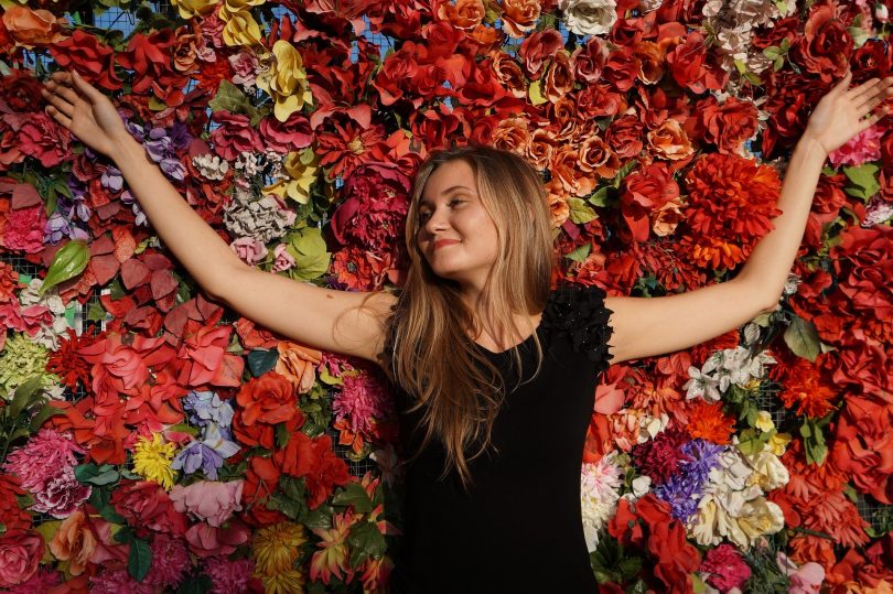 Imagem de uma linda mulher, feliz e com a sua autoestima elevada. Ela está deitada sobre um fundo todo florido.