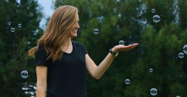 Mulher sorrindo em um jardim e segurando uma bolha de sabão