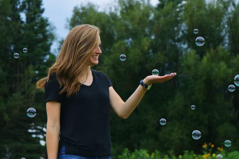 Mulher sorrindo em um jardim e segurando uma bolha de sabão