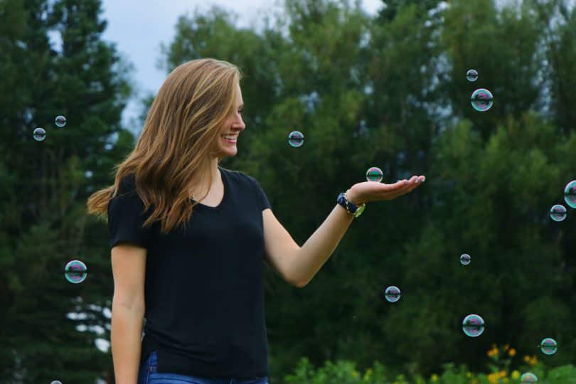 Mulher sorrindo em um jardim e segurando uma bolha de sabão