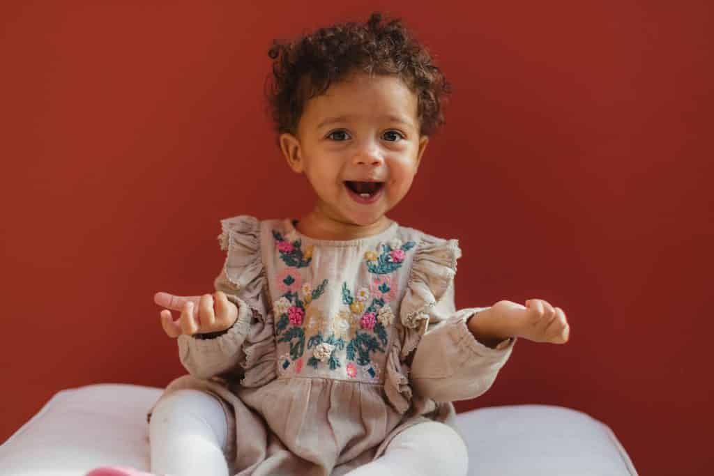 Bebê sorrindo sentada em uma almofada com as mãos levantadas