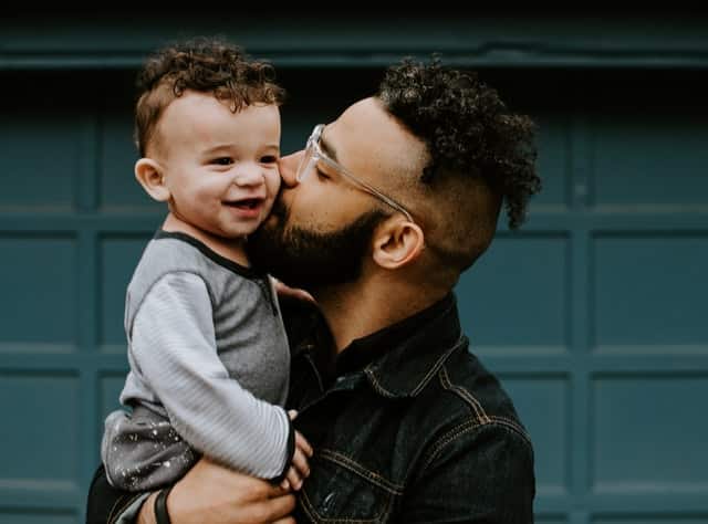 Pai negro beijando bochecha de filho branco