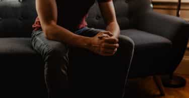 Homem sentado no sofá da sala com as mãos unidas