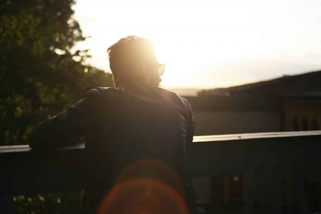 Homem apoiando seus braços em um uro olhando para o lado com a luz do sol em seu rosto