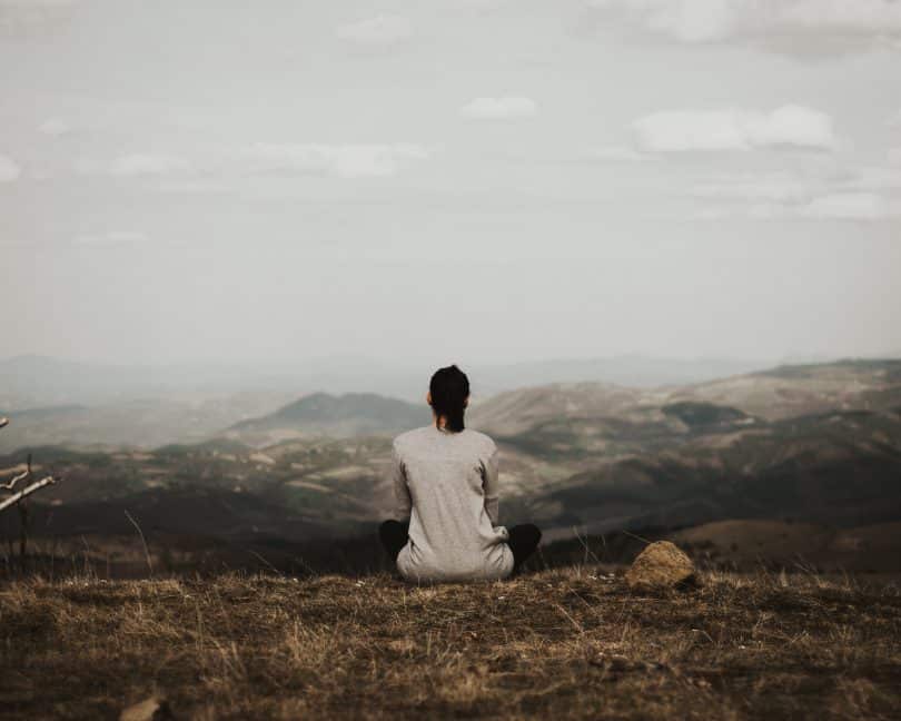 Mulher sentada em um gramado de uma montanha e olhando para o horizonte